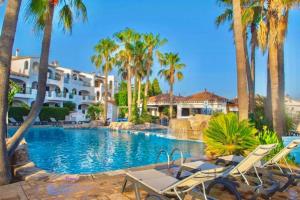a resort swimming pool with chairs and palm trees at Oasis Calan Porter con piscinas y junto la playa in Cala'n Porter