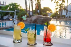 four cocktails sitting on a table next to a pool at Oasis Calan Porter con piscinas y junto la playa in Cala'n Porter