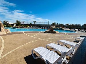 a swimming pool with two white chairs in a resort at Détente en 4 étoiles jusque 6 personnes, selon la dispo in Saint-Jean-de-Monts
