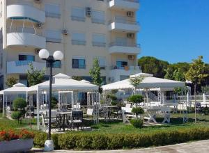 a hotel with tables and umbrellas in front of a building at Velipoja Apartment in Velipojë