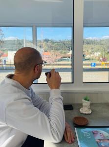 a man sitting at a desk looking out a window at Pensão Manalvo in Caxarias