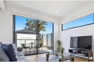 a living room with a tv and a large window at Domi Rentals - The Moorabbin Townhouse in Moorabbin