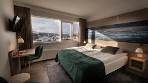 a bedroom with a bed and a desk and a window at Hotel Arctic in Ilulissat