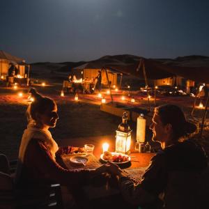 a man and woman sitting at a table in the desert at night at Sandrela Luxury Camp in Merzouga