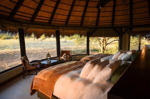 ein großes Bett in einem Zimmer mit einem großen Fenster in der Unterkunft Okonjima Luxury Bush Camp in Otjiwarongo