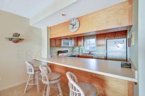 a kitchen with a counter with stools and a clock on the wall at Oceanview Amelia South Condo in Fernandina Beach