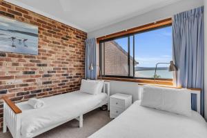 a bedroom with two beds and a brick wall at Waves on Winnunga in Pambula Beach +21 photos