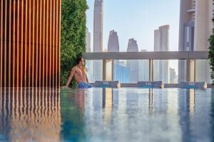 ドバイにあるWaldorf Astoria Dubai International Financial Centreの都会のスイミングプールに座る男