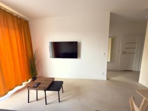 a living room with a table and a tv on a wall at Apartament Diuna z dostępem do basenu, siłowni, hali sportowej, sauny in Gąski