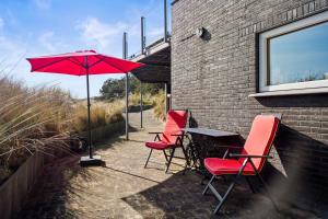 a table with red chairs and an umbrella on a patio at Co's Duyne - Beautiful studio near the dunes of Callantsoog in Callantsoog