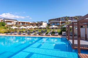 a swimming pool with lounge chairs and umbrellas at Isla Brown Chania Resort, Curio Collection by Hilton in Stavros