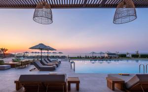 a pool with couches and chairs and a sunset at Isla Brown Chania Resort, Curio Collection by Hilton in Stavros