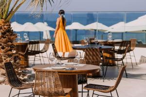 a woman in a yellow dress walking past tables and chairs at Isla Brown Chania Resort, Curio Collection by Hilton in Stavros