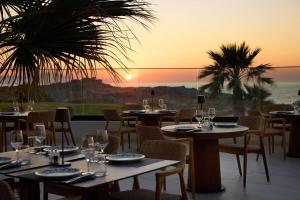 a restaurant with tables and chairs with a sunset in the background at Isla Brown Chania Resort, Curio Collection by Hilton in Stavros