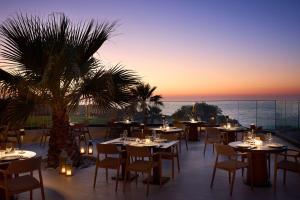a restaurant with tables and chairs and a palm tree at Isla Brown Chania Resort, Curio Collection by Hilton in Stavros