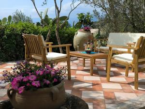 a patio with three chairs and a table and flowers at Splendida villa in riva al mare in Orosei