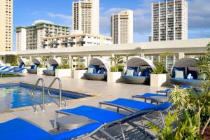 檀香山Hilton Waikiki Beach Resort & Spa的一座带蓝色躺椅的游泳池,位于大楼旁