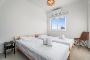 Modern seaview apartment in the heart of Agia Napa في أيا نابا: سريرين في غرفة بها نافذة وكرسي