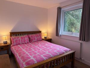 a bedroom with a bed with a pink comforter and a window at Highland Hideaway in Fort William