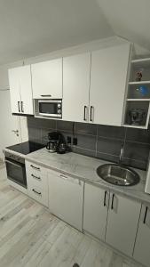 a kitchen with white cabinets and a sink and a microwave at Apartment Gradina in Korenica