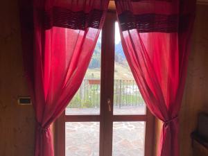 ein Fenster mit roten Vorhängen und Blick auf einen Balkon in der Unterkunft Villa Avio in Temù + 1 Foto