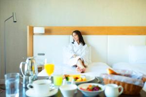 a woman sitting on a bed with a tray of food at Grand Nikko Tokyo Daiba in Tokyo