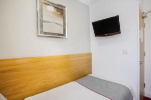 a room with a bed and a tv on a wall at London Guest House by OYO - Acton in London