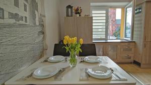 a table with two plates and a vase with yellow flowers at Apartament Leliwa - Centrum - blisko dworca PKP - blisko Starówki - restauracje i sklepy w pobliżu - pierwsze piętro - możliwy kurs na lotnisko -faktura - kawa - herbata - English in Tarnów