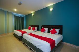 two beds with red and white pillows in a room at Hotel O Hotel Orchard Inn in Lumut