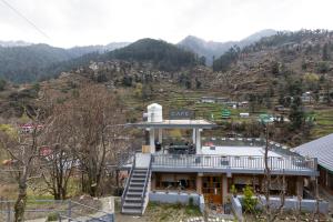 a building on a hill with mountains in the background at Eden Stay & Cafe in Jibhi
