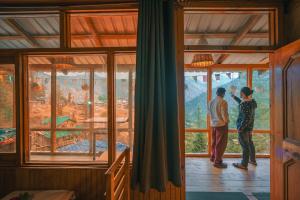 due persone in piedi in una stanza che guardano fuori da una finestra di Negi Farmhouse Shangarh a Sainj