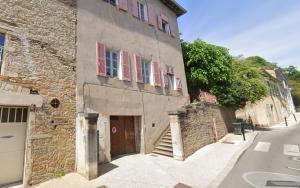 an old stone building with pink shutters on a street at La White box in Trévoux
