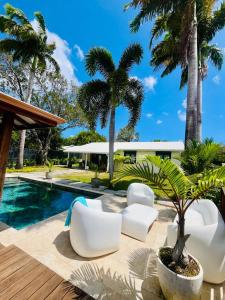 a patio with white chairs and a swimming pool with palm trees at Villa Boheme O Lagon in Le François