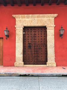 a red wall with a wooden door and two lights at Tranquila y cerca de la magia in Cartagena de Indias