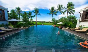 una piscina en un complejo con gente en el agua en Legacy Hoi An Resort en Hoi An