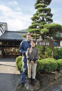 a man and a woman standing in front of a tree at Kamesei Ryokan in Chikuma