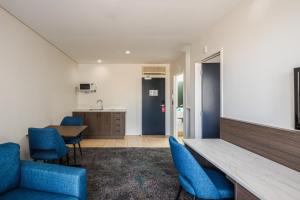 a room with blue chairs and a table and a kitchen at Heartland Hotel Auckland Airport in Auckland