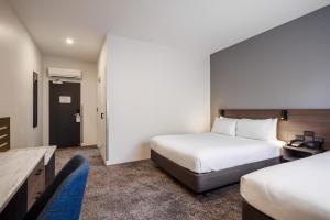 a hotel room with two beds and a desk and chair at Heartland Hotel Auckland Airport in Auckland