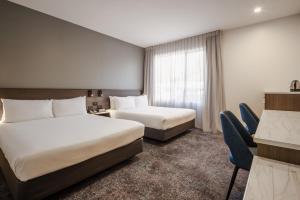 a hotel room with two beds and a desk at Heartland Hotel Auckland Airport in Auckland