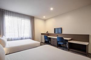 a hotel room with two beds and a desk at Heartland Hotel Auckland Airport in Auckland