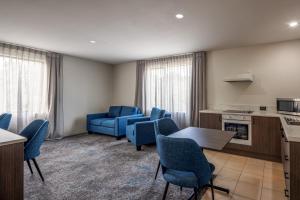 a living room with blue chairs and a kitchen at Heartland Hotel Auckland Airport in Auckland