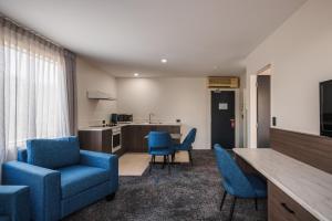 a living room with blue chairs and a kitchen at Heartland Hotel Auckland Airport in Auckland