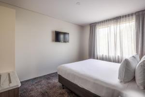 a white bedroom with a bed and a window at Heartland Hotel Auckland Airport in Auckland