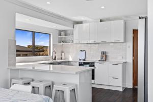 una cocina blanca con armarios y taburetes blancos en Sandbanks - Papamoa Beachfront Holiday Home, en Papamoa