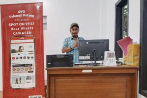 a man standing at a desk with a computer at Hotel O Desa Wisata Kawasen in Padaherang