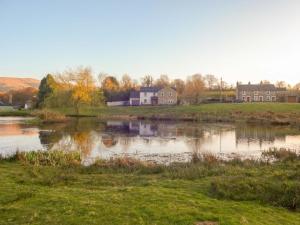 a pond in a field with houses in the background at Greenside Cottage Caldbeck in Caldbeck