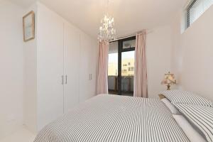a white bedroom with a bed and a chandelier at Muizenberg Apartment in Muizenberg +14 photos
