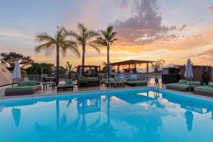 a swimming pool with palm trees and a sunset at Bella Vista Hôtel, Suites & Maisons in Porticcio