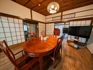 a dining room with a wooden table and a flat screen tv at 1棟貸切で家族仲間と焚火バーベキューを楽しめる古民家NanasawaBasshouse in Atsugi