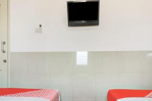 a room with two beds and a tv on the wall at OYO 91316 Hh Guest House Makassar in Makassar